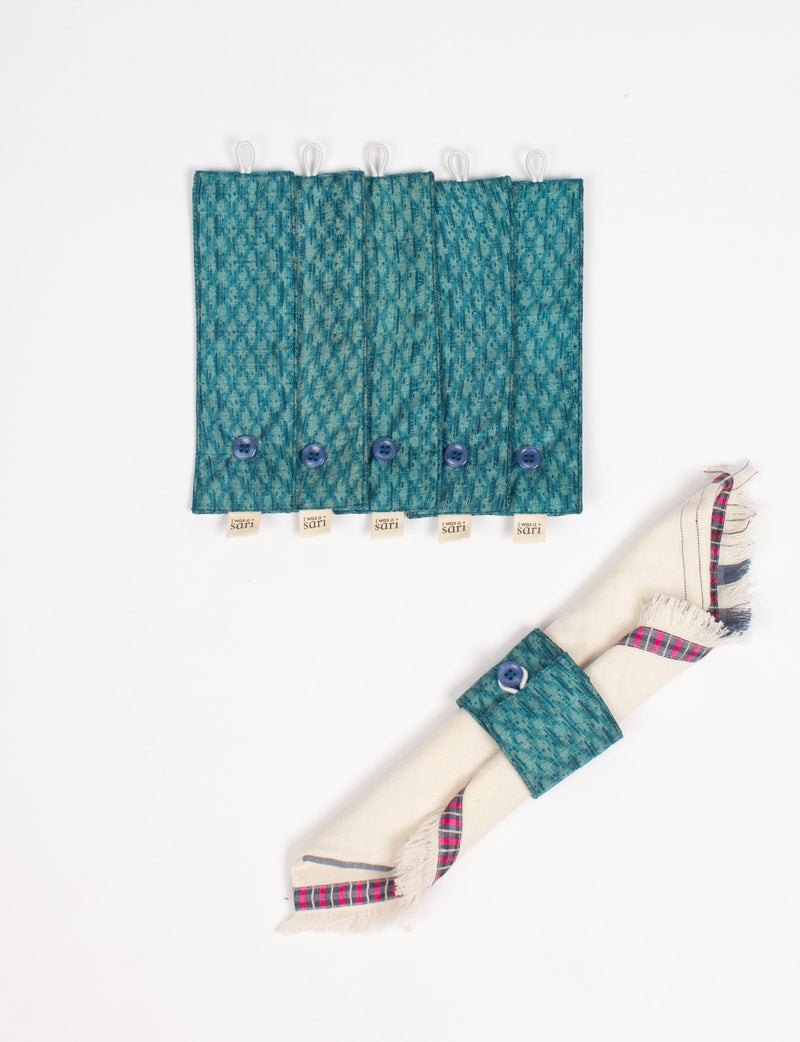 Set of six blue patterned fabric napkin rings with buttons and "I was a sari" tags, one holding a folded napkin