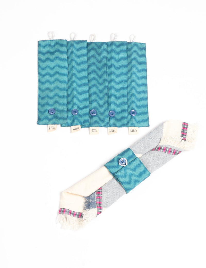 Set of six teal blue fabric napkin rings with wavy pattern, blue buttons, and "I was a sari" tags, shown flat and on a napkin