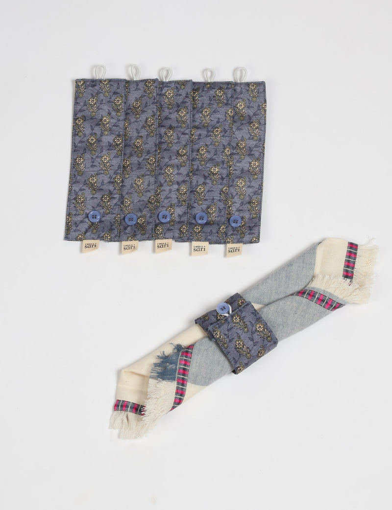 Set of six blue floral fabric napkin rings with buttons and "I was a sari" tags, shown flat and holding a folded napkin