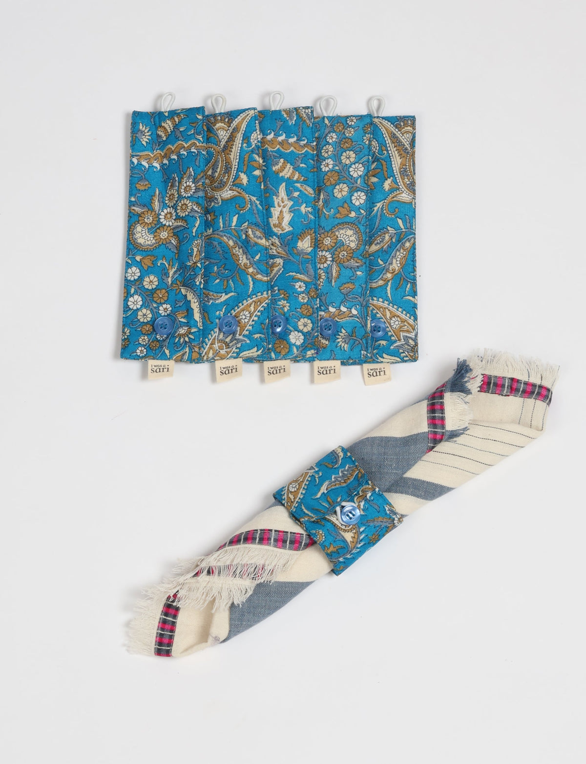 Set of six blue paisley patterned fabric napkin rings with buttons and "I was a sari" tags, shown flat and on a rolled napkin