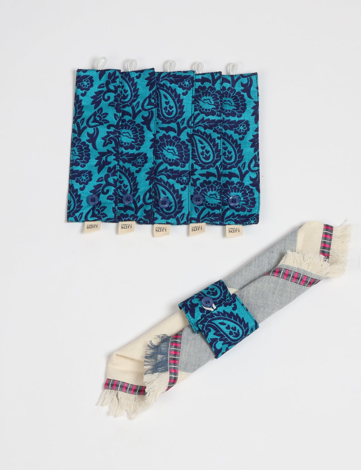 Set of six blue and teal floral patterned fabric napkin rings with buttons, one shown holding a folded napkin