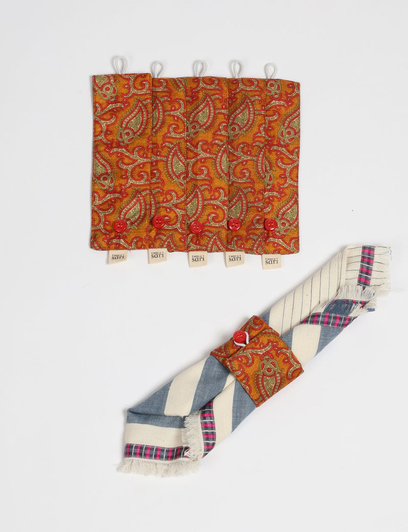 Set of six orange paisley fabric napkin rings with red buttons and white loops, one shown holding a striped napkin