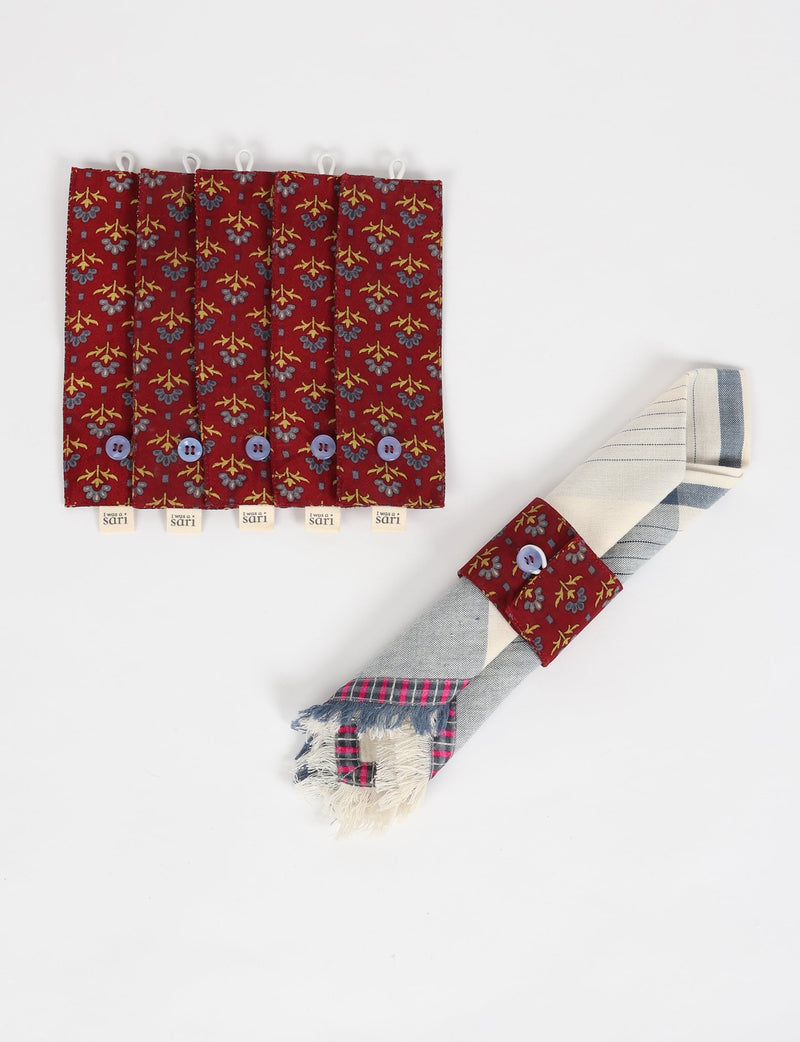 Set of six red floral fabric napkin rings with blue buttons and "I was a sari" tags, one holding a folded napkin
