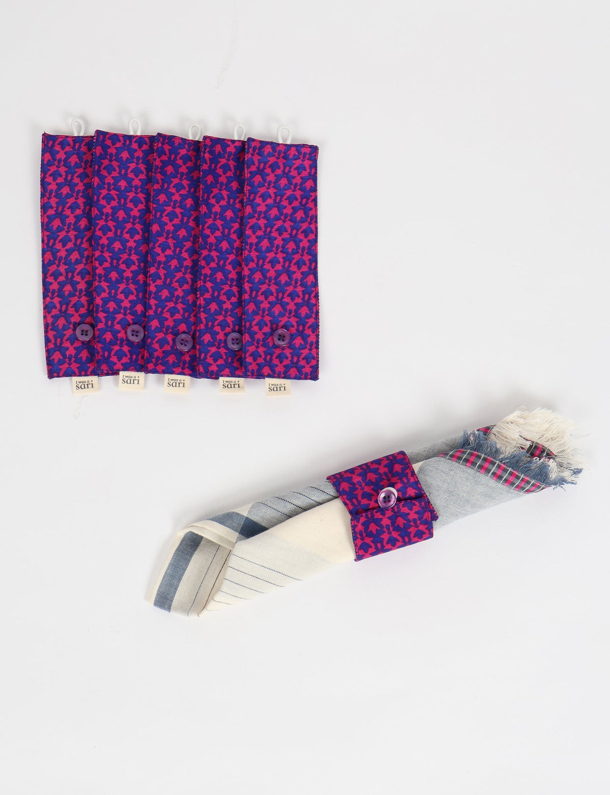 Set of six blue and pink patterned fabric napkin rings with purple buttons, one holding a folded striped napkin with fringe