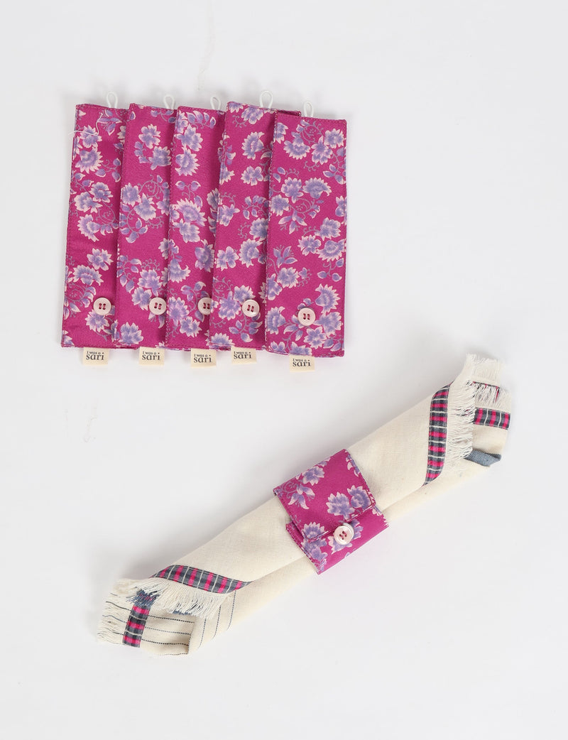Set of six pink floral fabric napkin rings with button closures, shown flat and one wrapped around a cream napkin with plaid trim