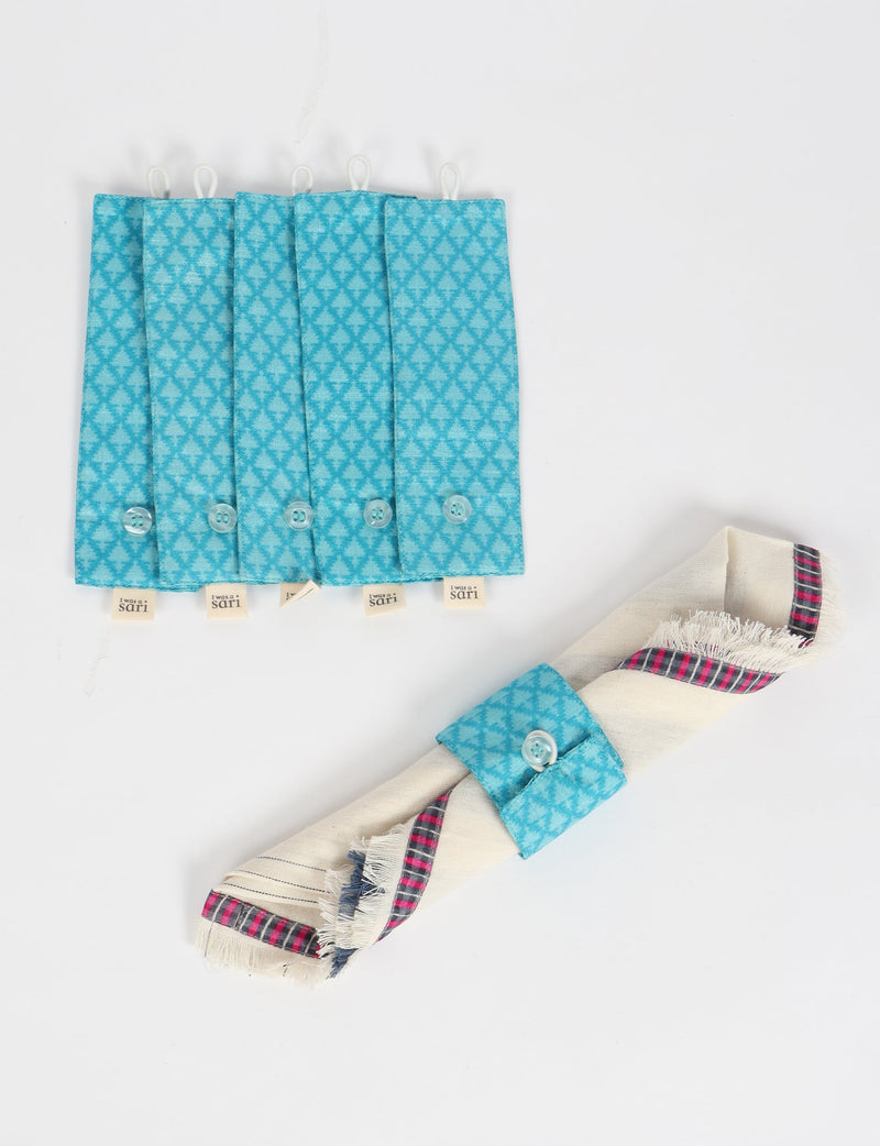 Set of six blue napkin rings with micro diamond pattern, button closure, and "I was a sari" label, shown flat and on a napkin