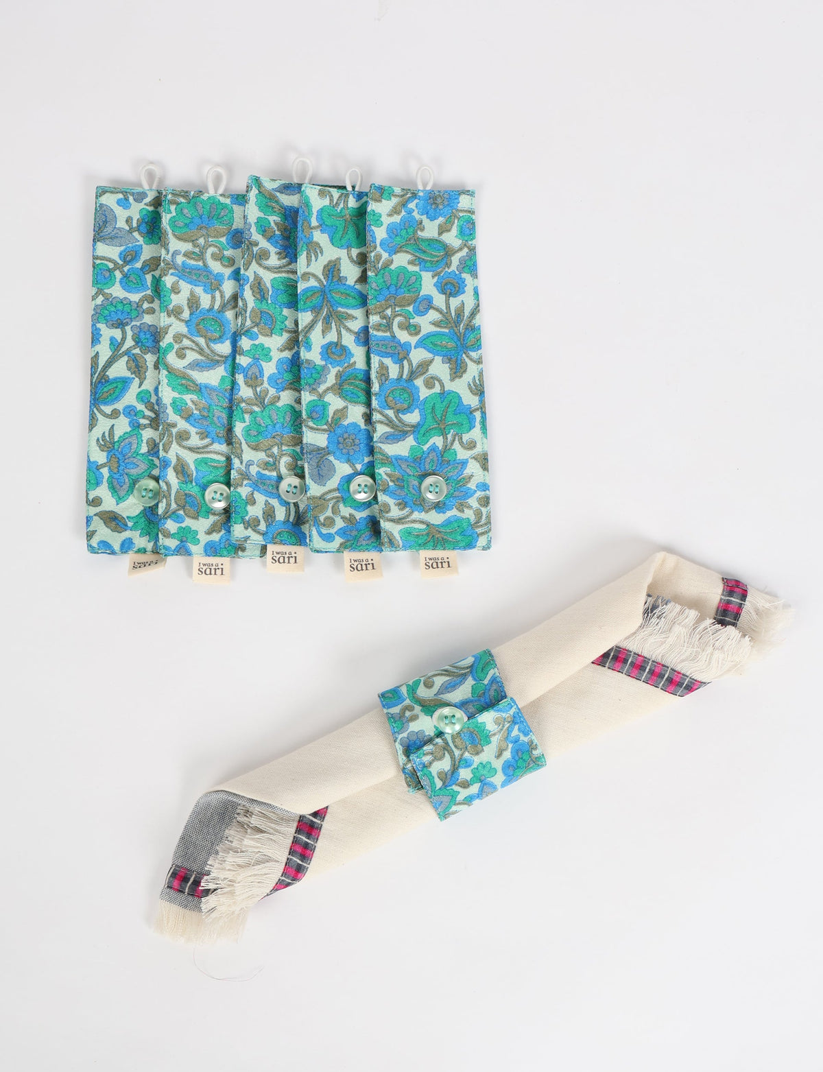 Set of six blue floral fabric napkin rings with button closures, one shown securing a cream napkin with plaid trim
