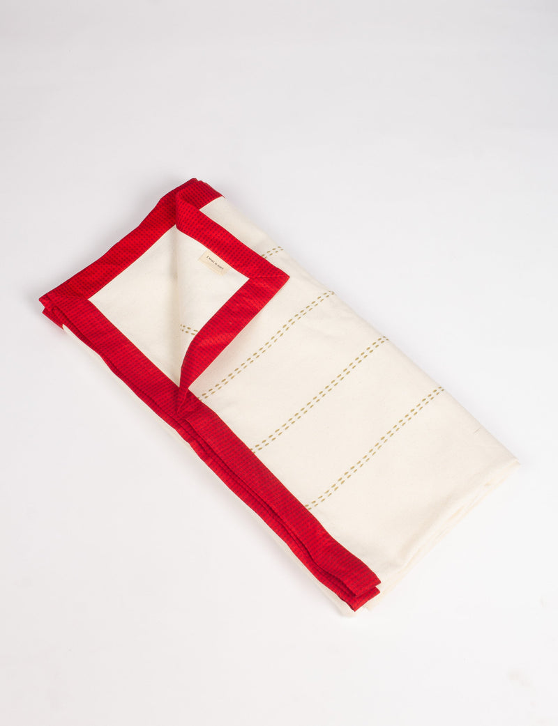 Folded cotton sofa throw with cream base, red broad sari edging, and stitched horizontal lines on a white background