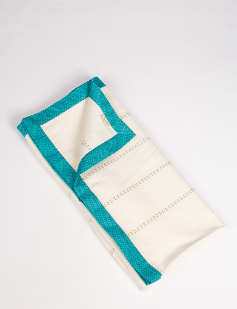Folded cotton sofa throw in off-white with broad blue sari edging and subtle stitched lines, flat lay view