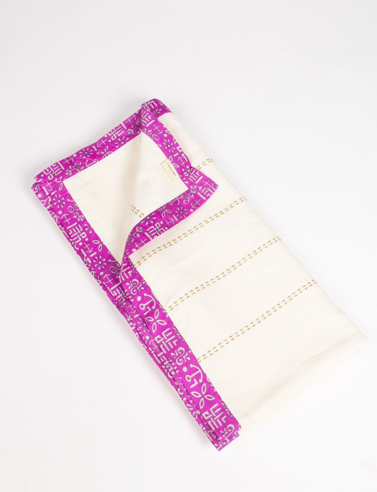 Folded white cotton sofa throw with pink sari patterned broad edging and stitched horizontal lines on white background