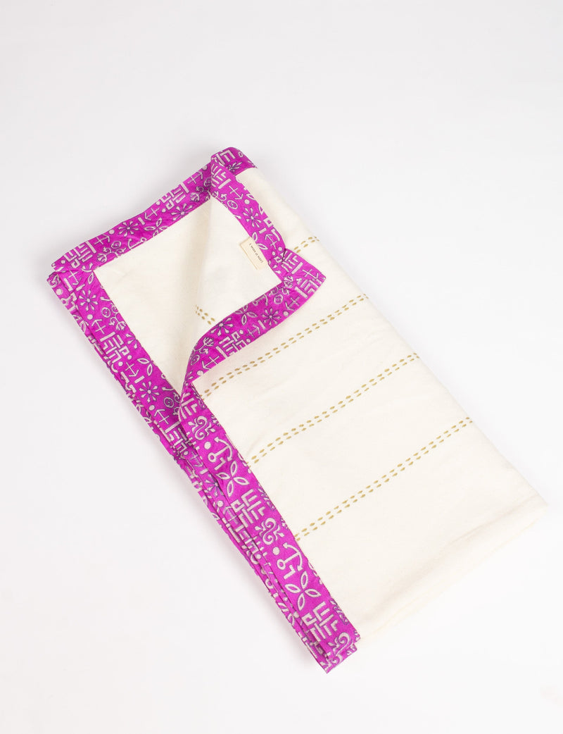 Folded white cotton sofa throw with pink sari patterned broad edging and stitched horizontal lines on white background