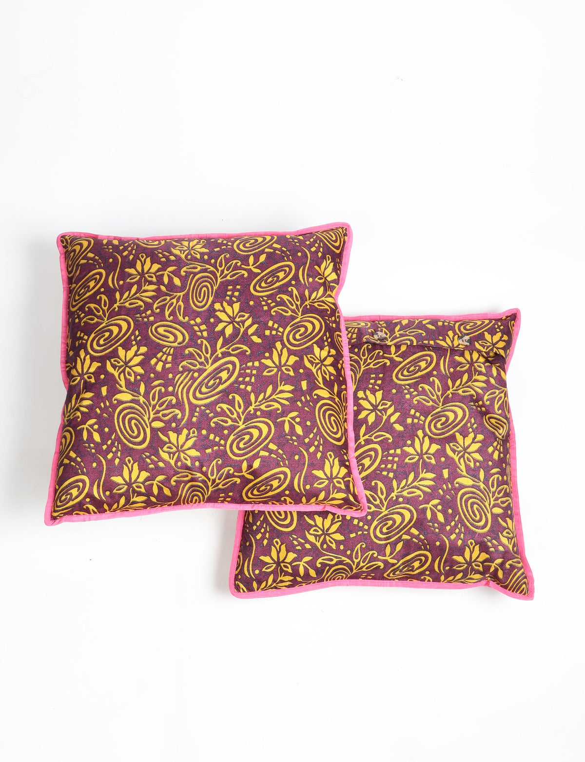Set of two red cushion covers with yellow tropical floral and swirl patterns, pink piping edges, shown flat on white background