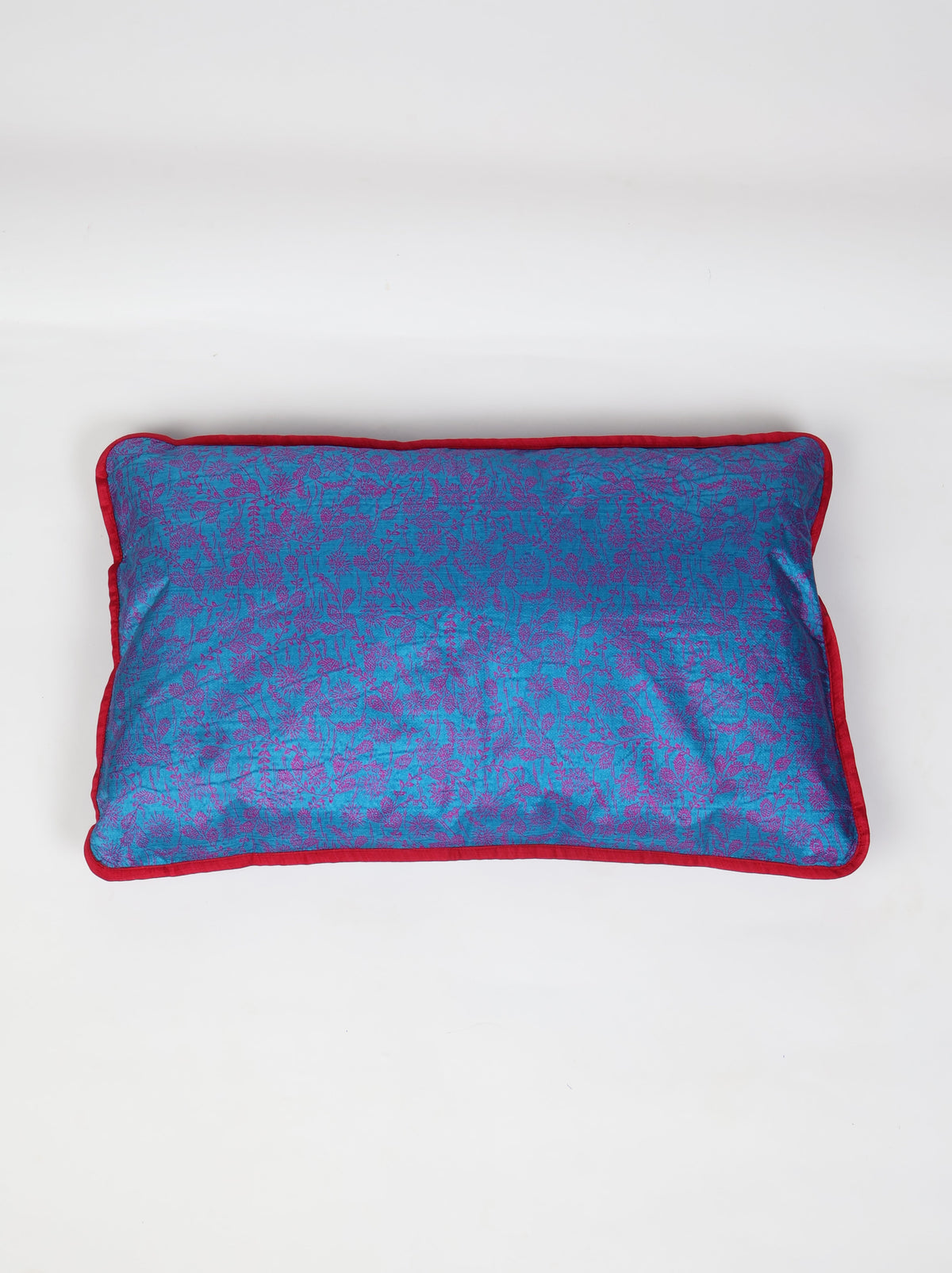 Rectangular lumbar cushion cover in blue cotton with purple floral print and red piping edge, flat lay view