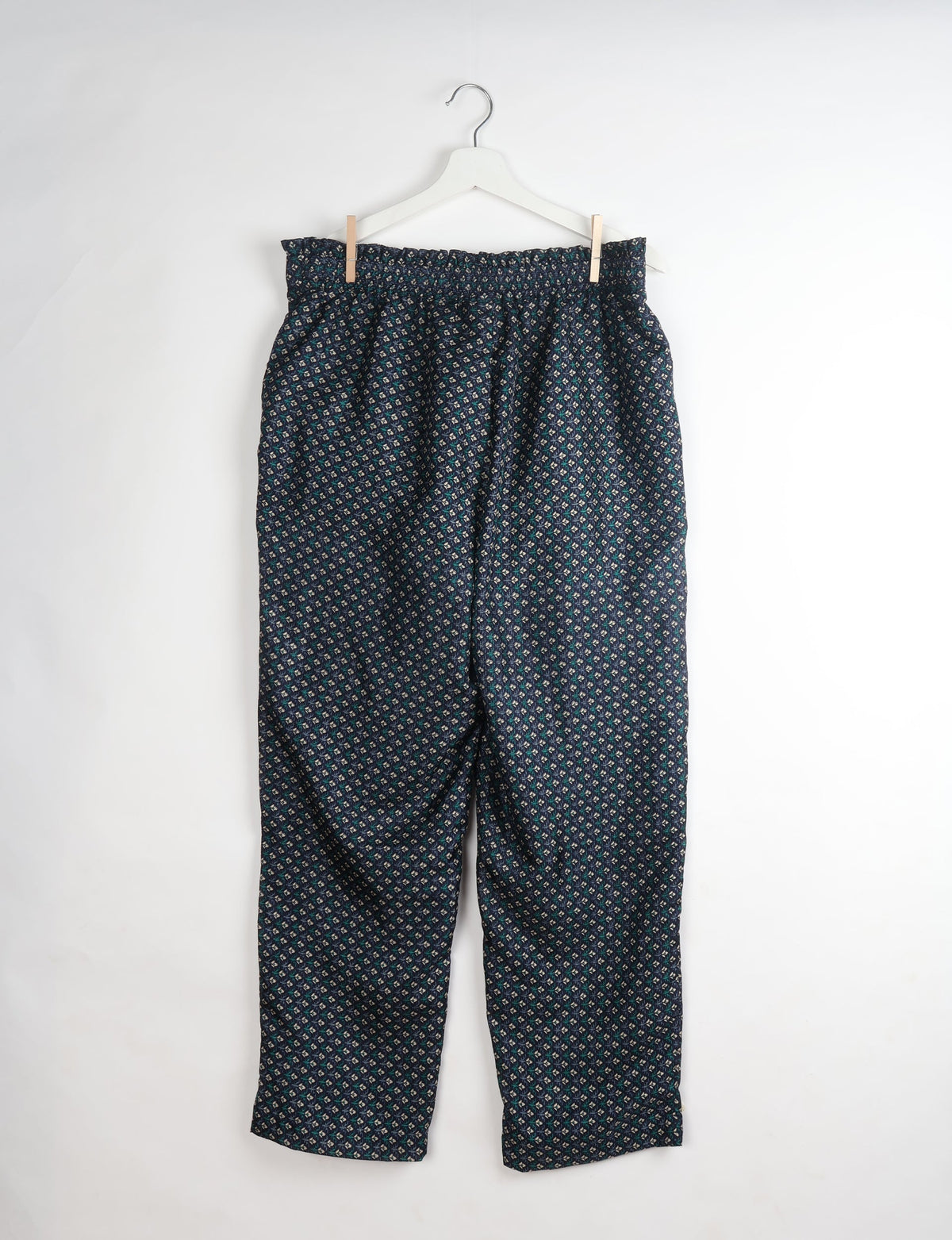 Blue paperbag high-waisted pull-on pants with a small floral micro design, hanging on a white hanger against a white background