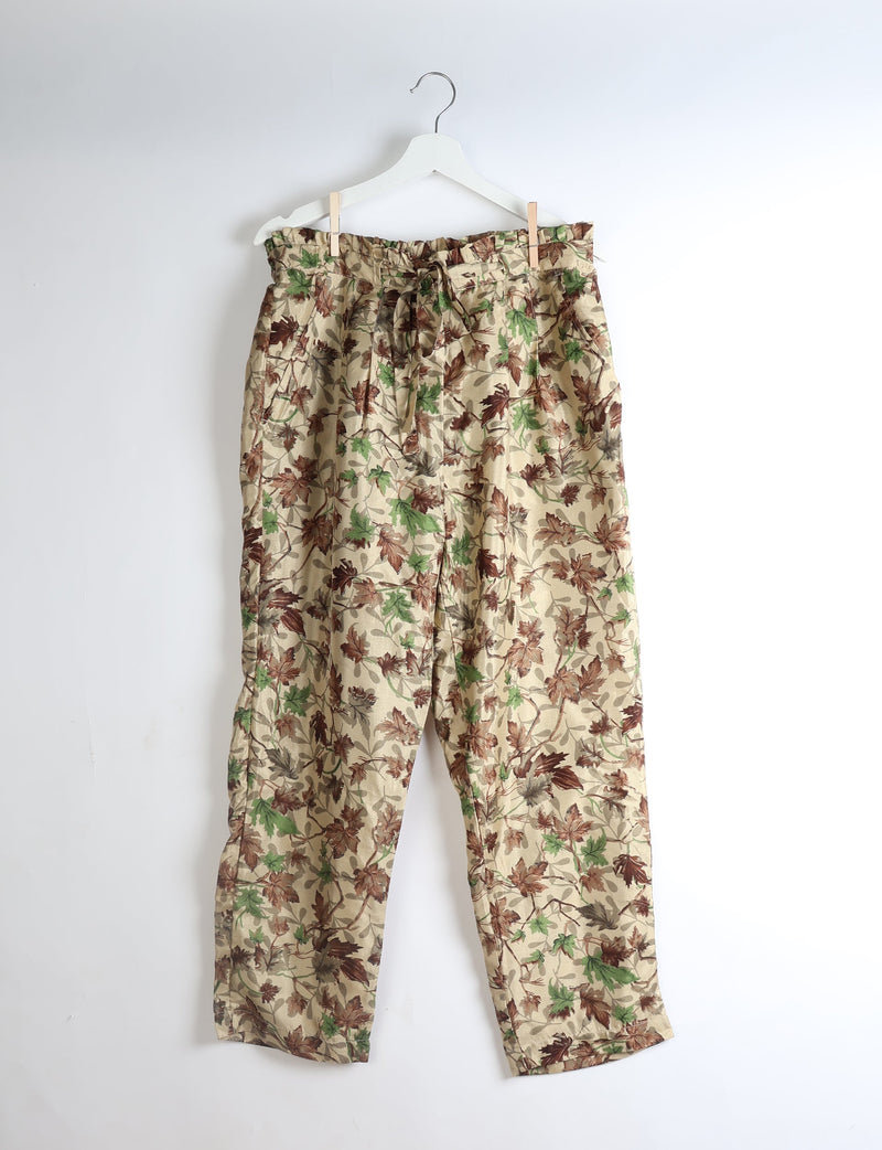 Beige paperbag high-waisted pull-on pants with green and brown leaf print, front pockets, and waist tie, hanging on white hanger