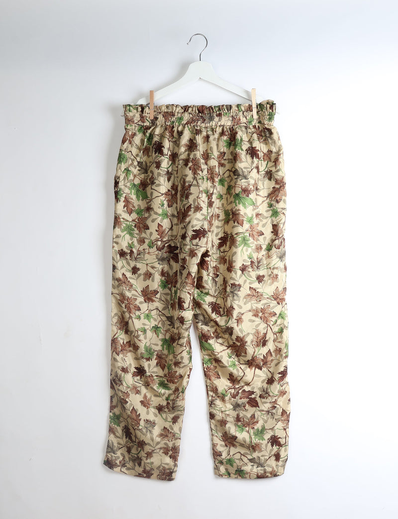 Beige paperbag high-waisted pull-on pants with brown and green leaf print, hanging on white hanger against white background