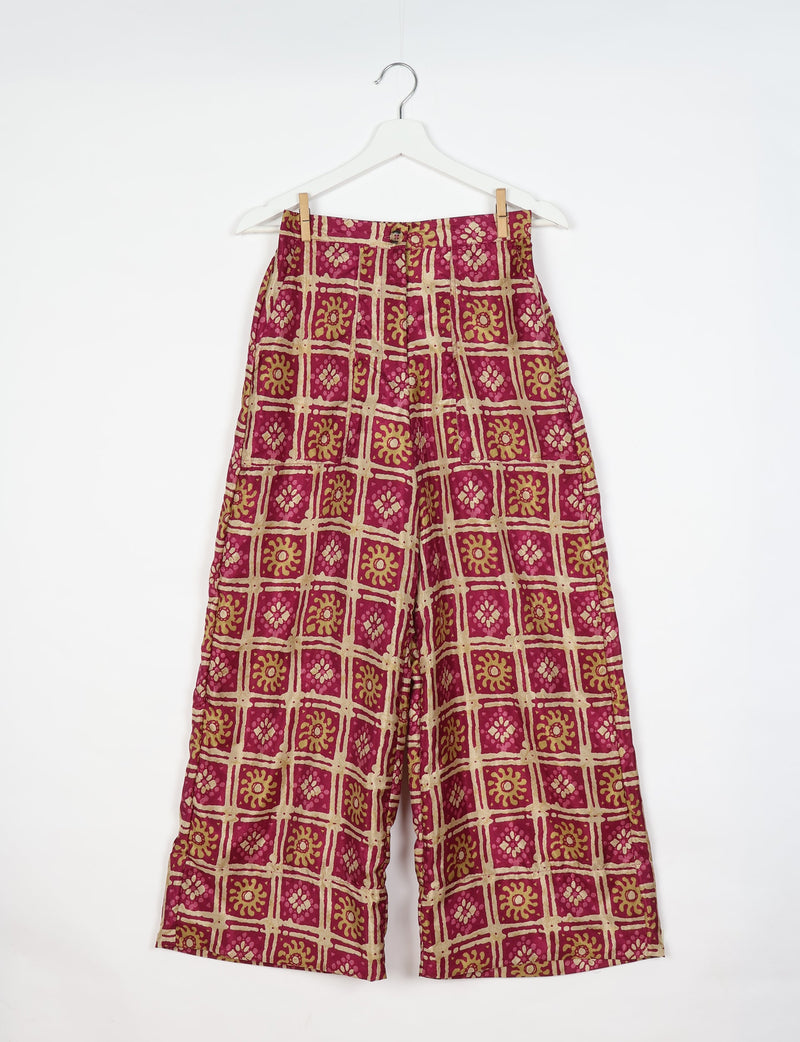 Pink wide-leg pants with beige and mustard Indian ethnic square and floral block print, hanging on white hanger