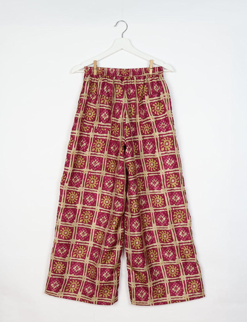 Pink wide leg pants with beige and olive green floral grid print, elastic waistband, and patch pockets, hanging on white hanger