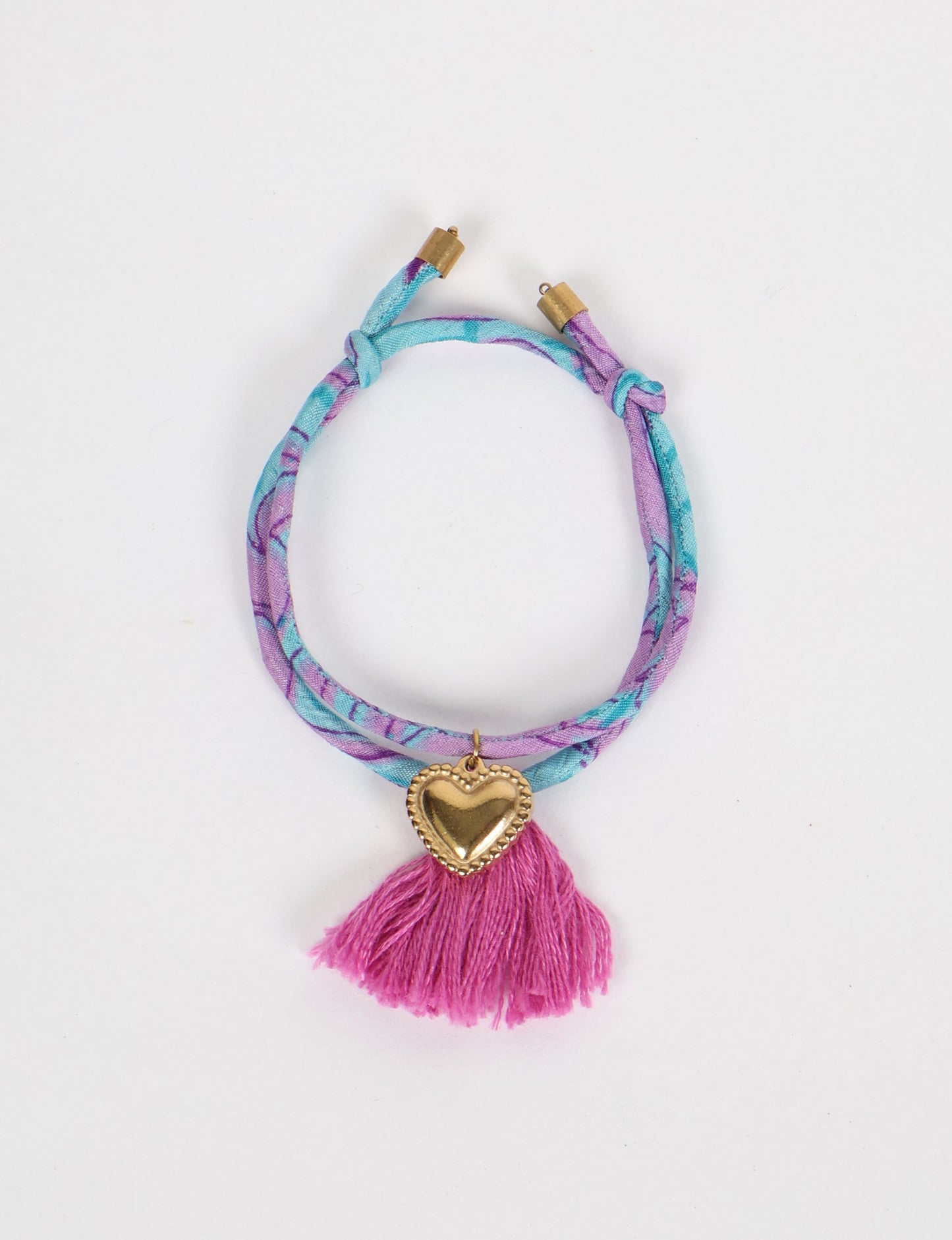 Handmade rope bracelet from recycled sari fabric with gold heart charm and tassels—eco friendly cloth, climate neutral fashion, and upcycled women’s clothing.