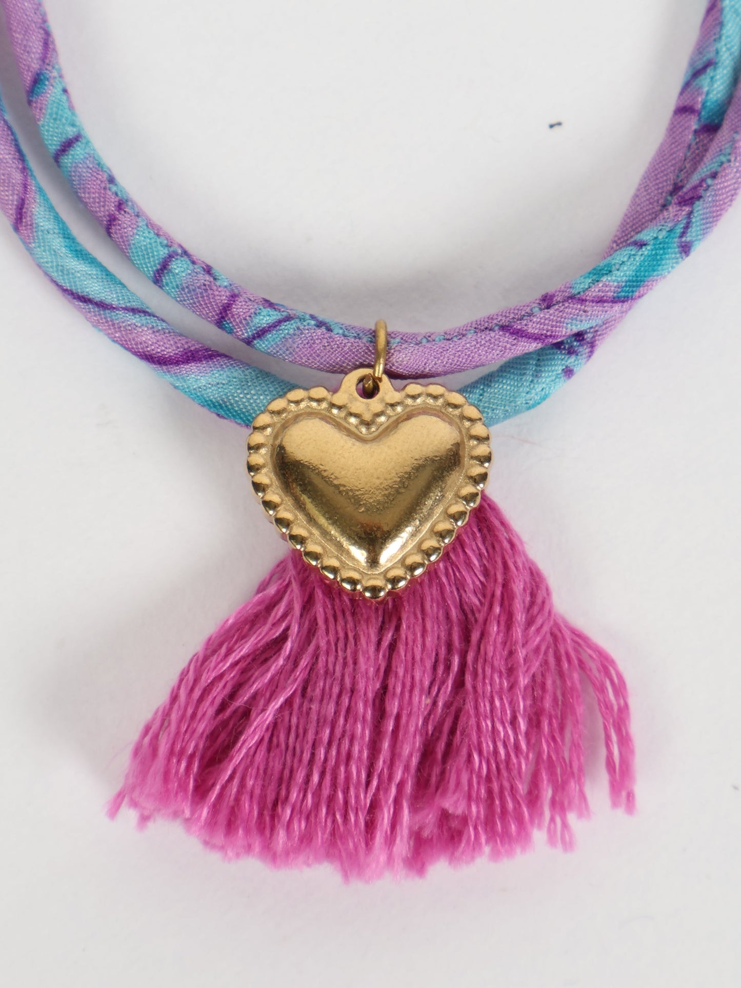 Handmade rope bracelet from recycled sari fabric with gold heart charm and tassels—eco friendly cloth, climate neutral fashion, and upcycled women’s clothing.