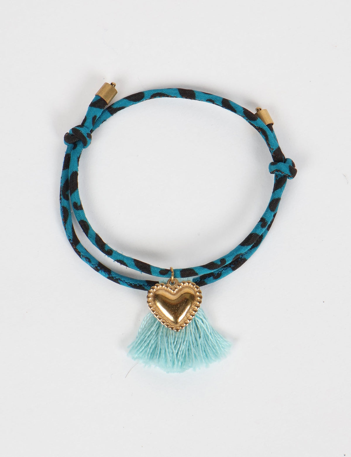 Blue and black abstract patterned rope bracelet with gold heart charm and light blue tassel, flat lay view