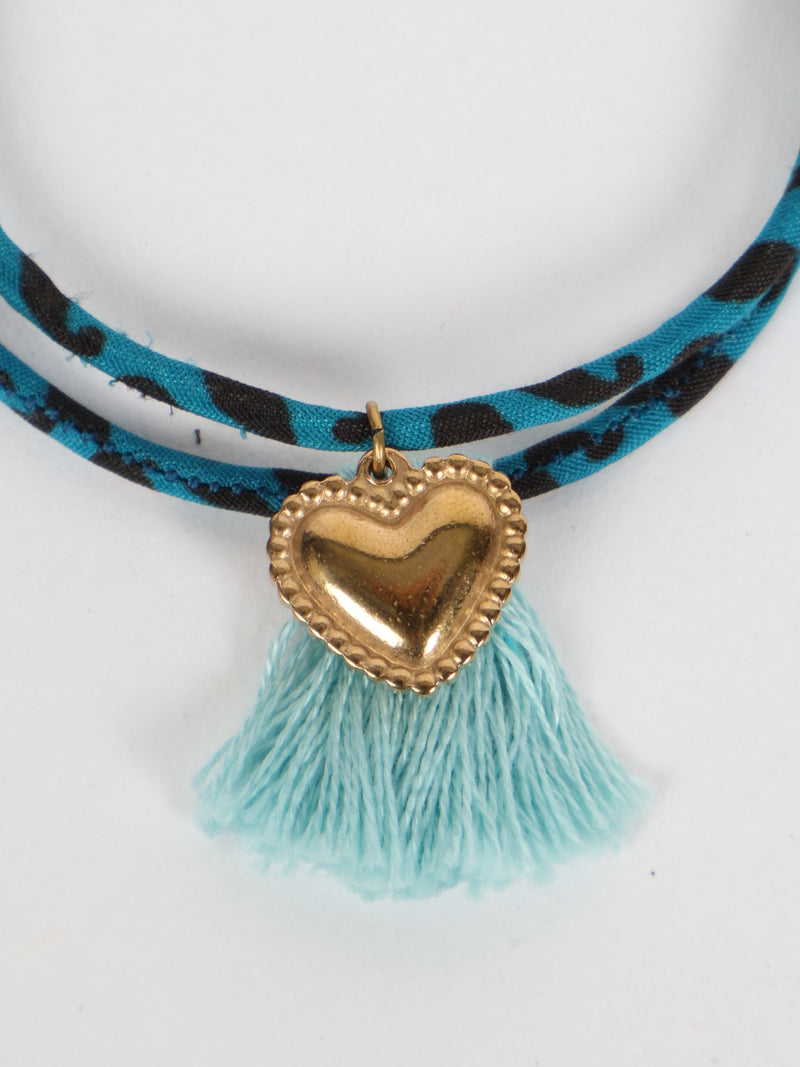 Black and blue patterned rope bracelet with gold heart charm and light blue tassels, shown in close-up front view