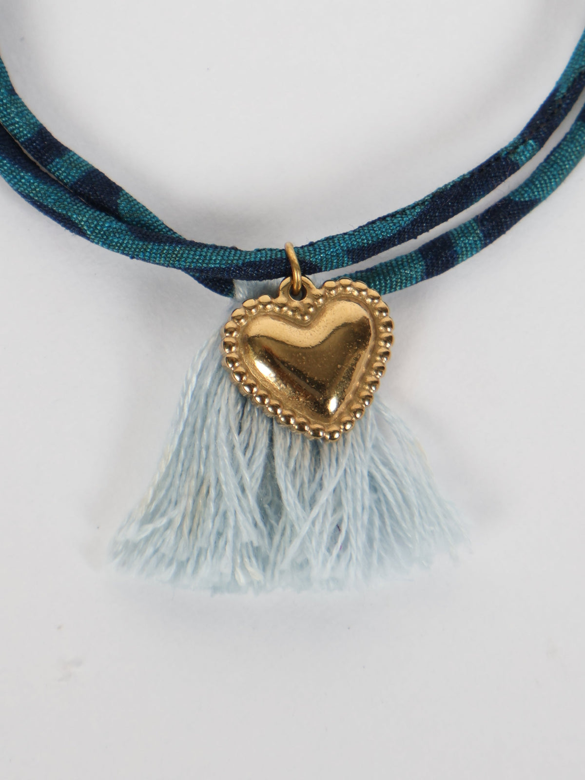 Blue and navy abstract patterned rope bracelet with light blue tassels and a gold heart charm pendant, front view