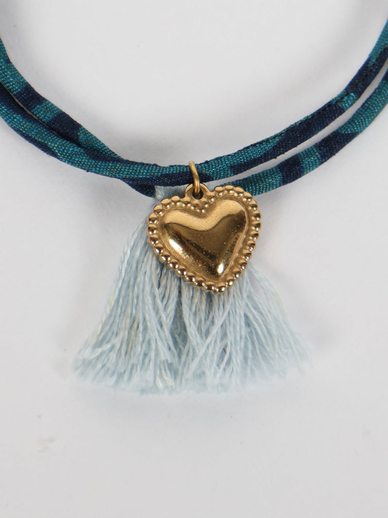 Blue and navy abstract patterned rope bracelet with light blue tassels and a gold heart charm pendant, front view