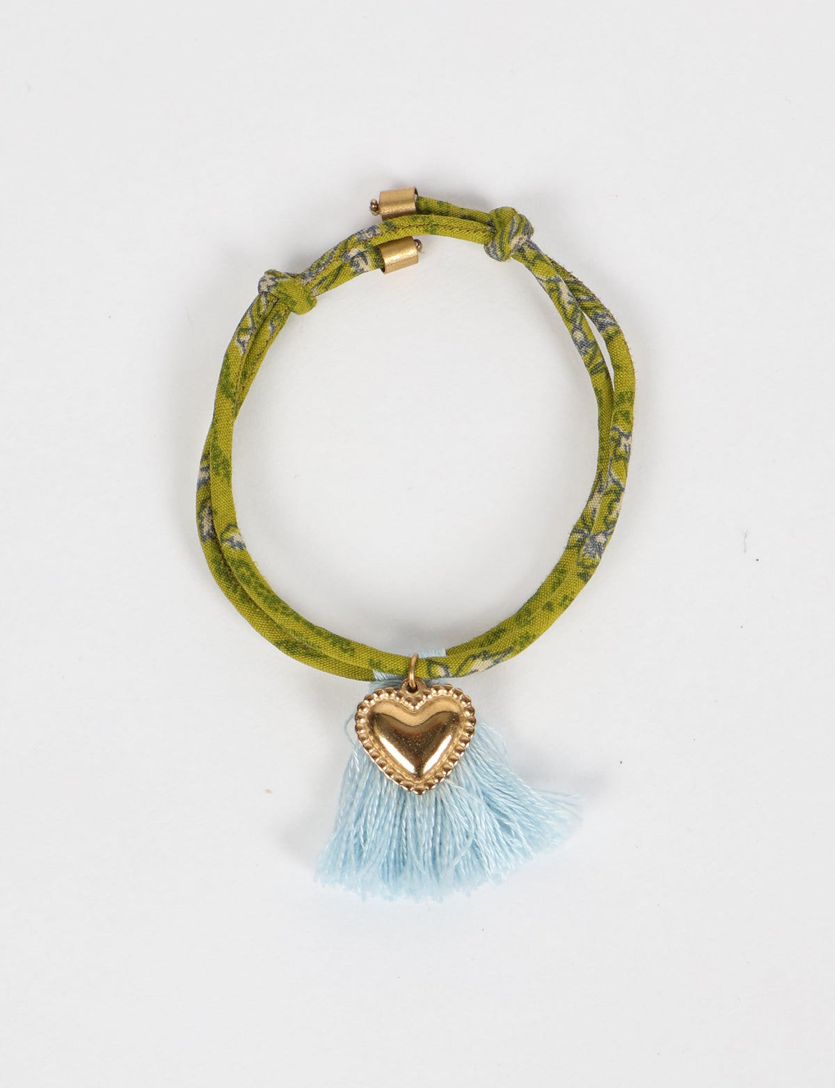 Green abstract patterned rope bracelet with gold heart charm and light blue tassels, flat lay view on white background