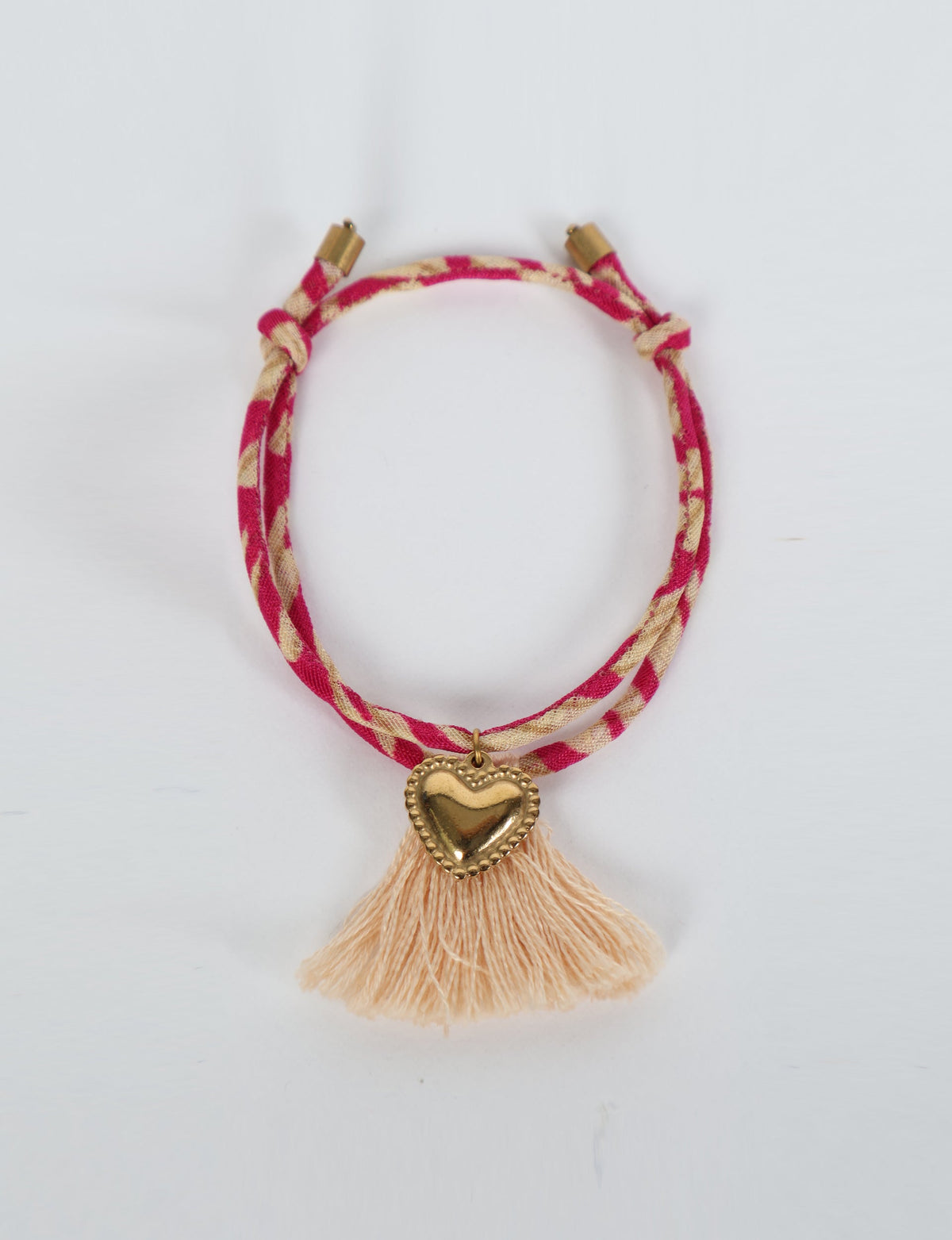 Pink and beige abstract patterned rope bracelet with gold heart charm and beige tassels, flat lay view on white background