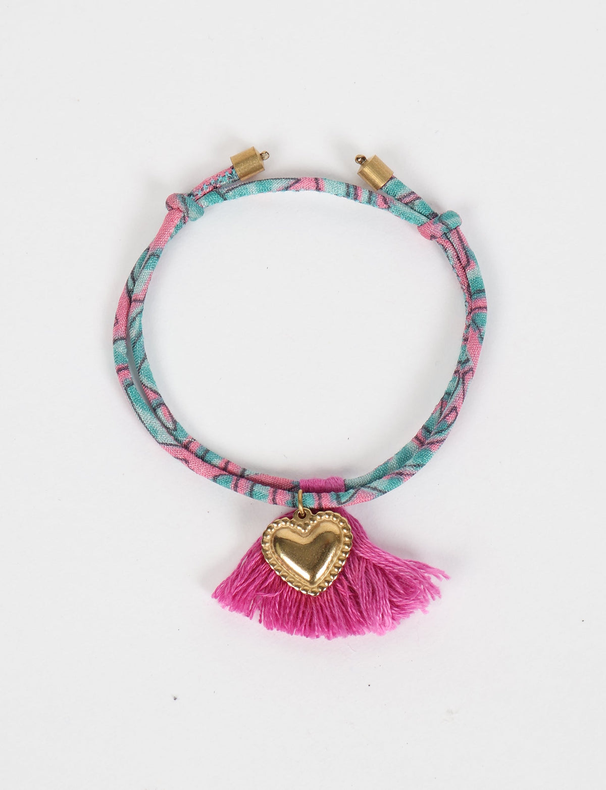 Pink and teal abstract patterned rope bracelet with gold heart charm and pink tassel, flat lay on white background