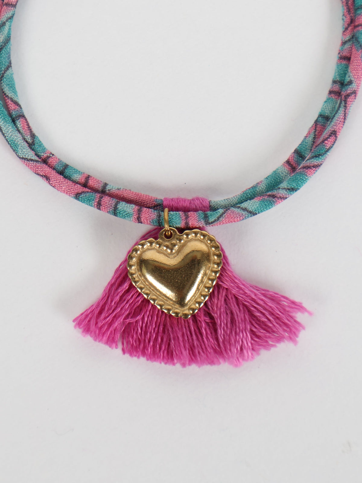 Pink and teal abstract patterned rope bracelet with gold heart charm and pink tassels, close-up front view on white background