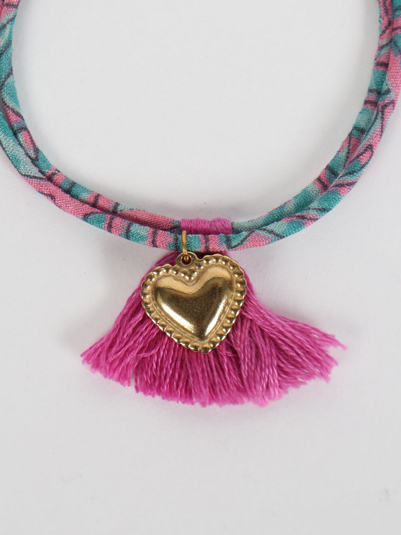 Pink and teal abstract patterned rope bracelet with gold heart charm and pink tassels, close-up front view on white background
