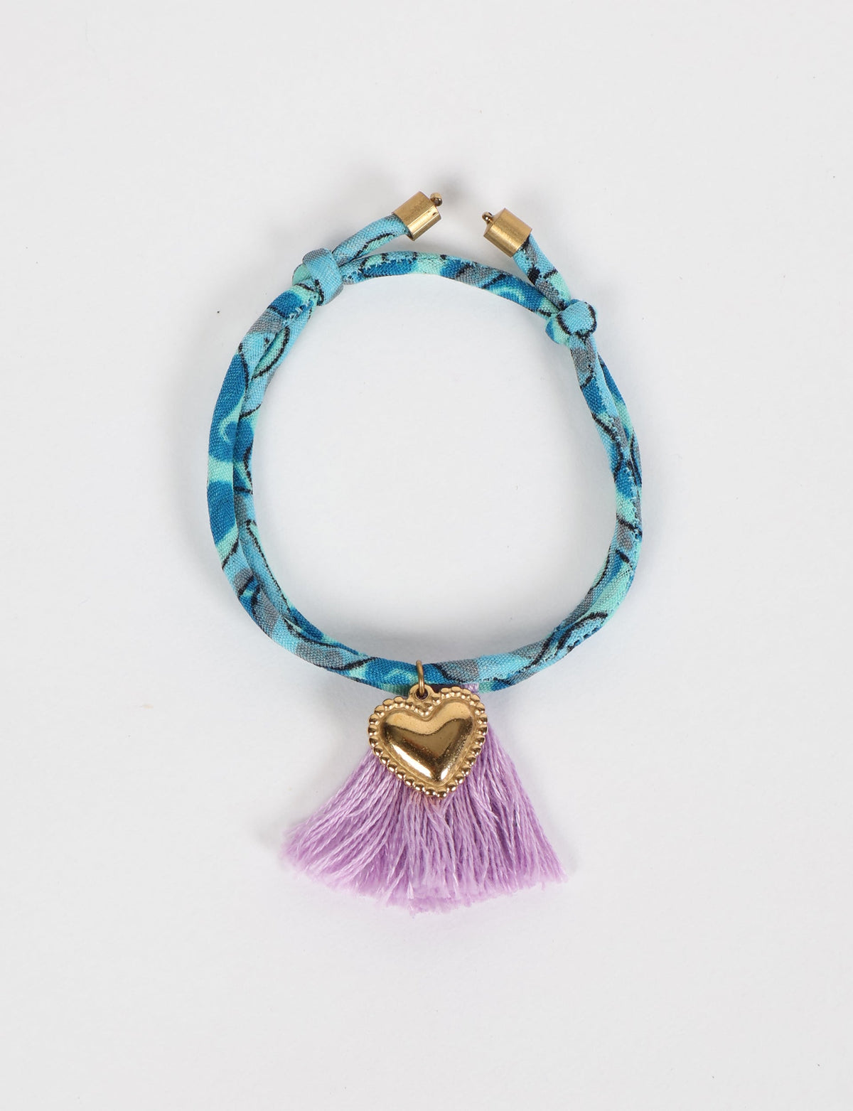 Blue patterned rope bracelet with gold heart charm and purple tassels, shown flat on white background