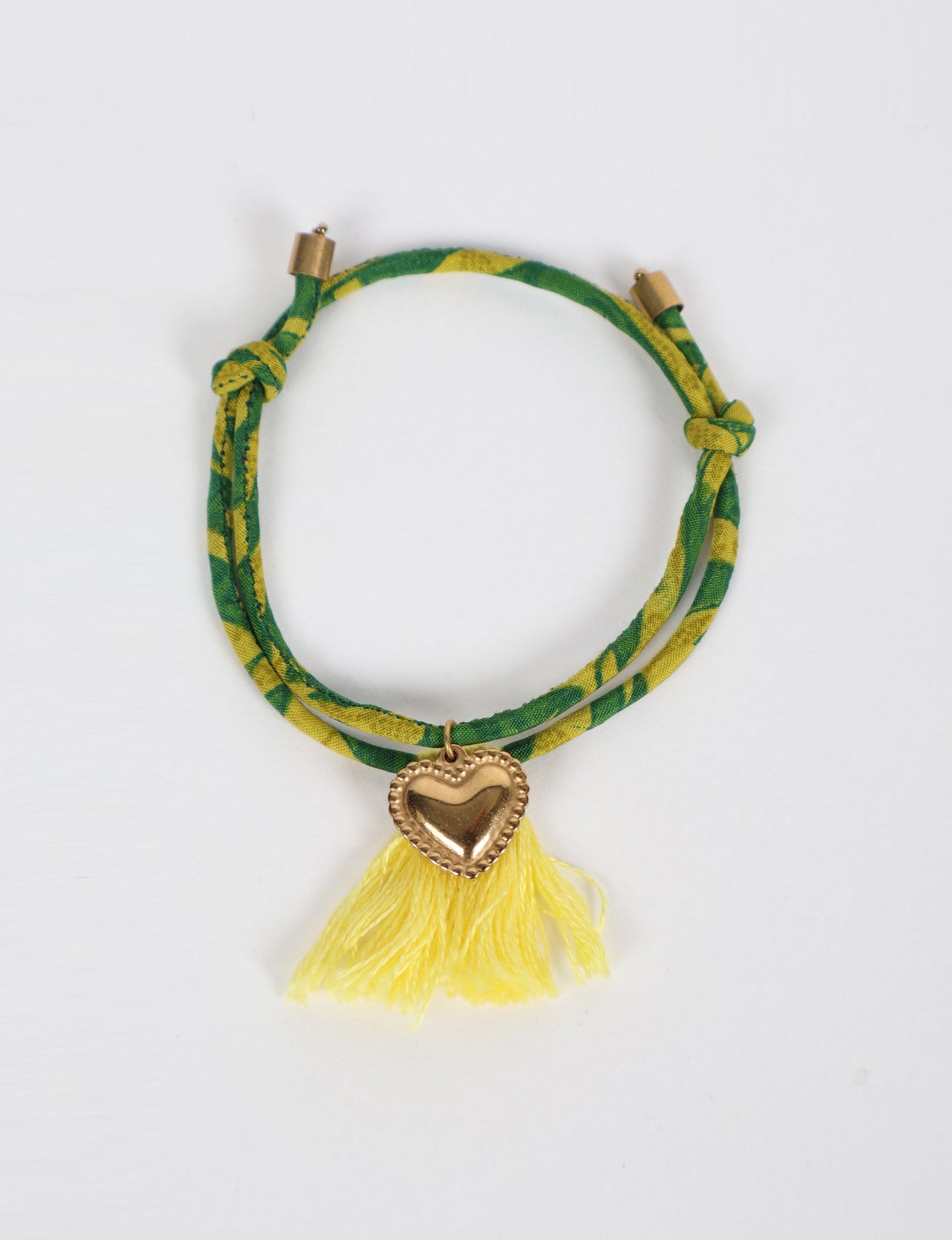 Handmade rope bracelet from recycled sari fabric with gold heart charm and tassels—eco friendly cloth, climate neutral fashion, and upcycled women’s clothing.