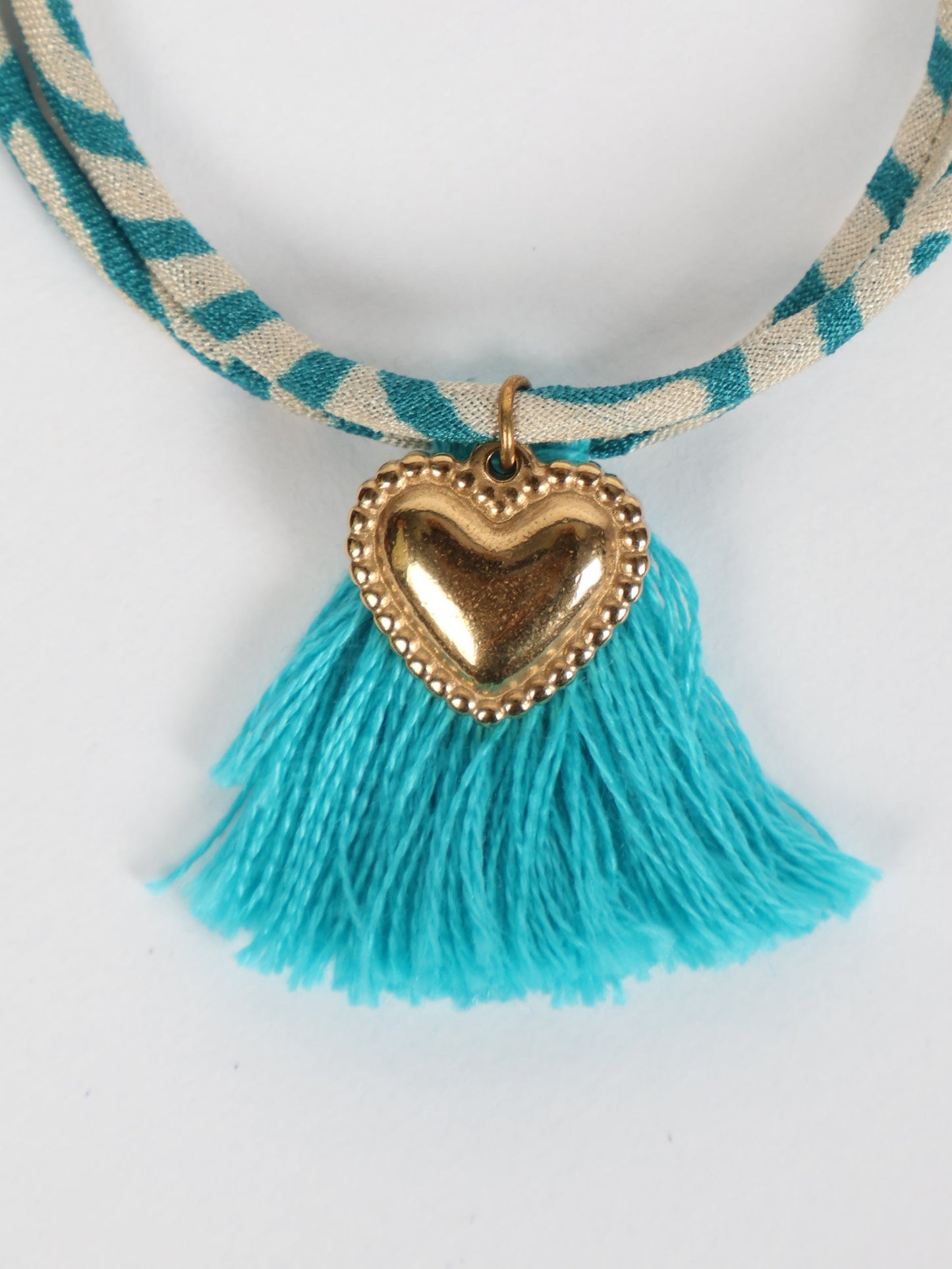 Handmade rope bracelet from recycled sari fabric with gold heart charm and tassels—eco friendly cloth, climate neutral fashion, and upcycled women’s clothing.