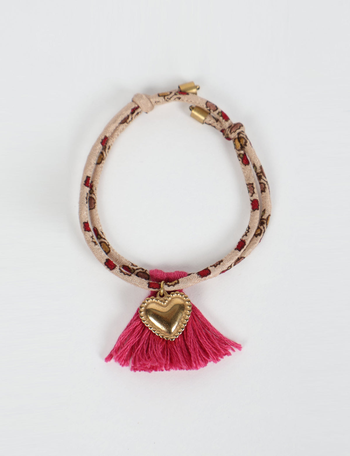 Beige rope bracelet with red and brown abstract pattern, gold heart charm, and pink tassel, flat lay view