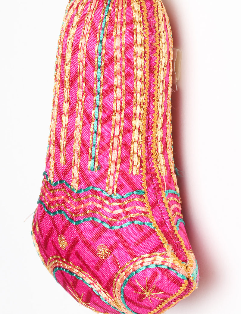 Close-up of a pink fabric bell ornament with gold, teal, and peach embroidered vertical stripes and floral patterns