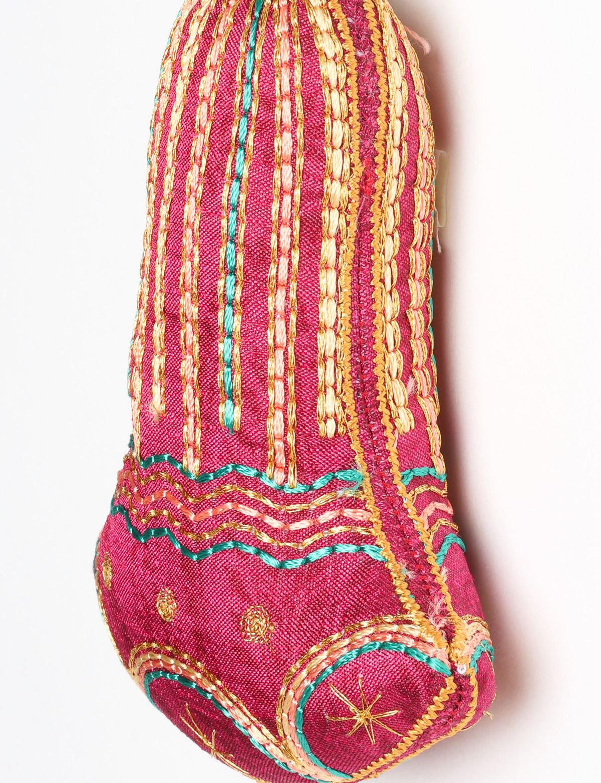 Close-up of a pink fabric bell ornament with gold, teal, and peach embroidered vertical stripes and floral patterns