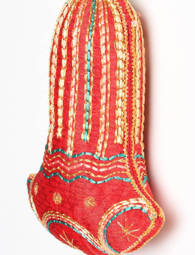 Close-up of a pink fabric bell ornament with gold, teal, and peach embroidered vertical stripes and floral patterns