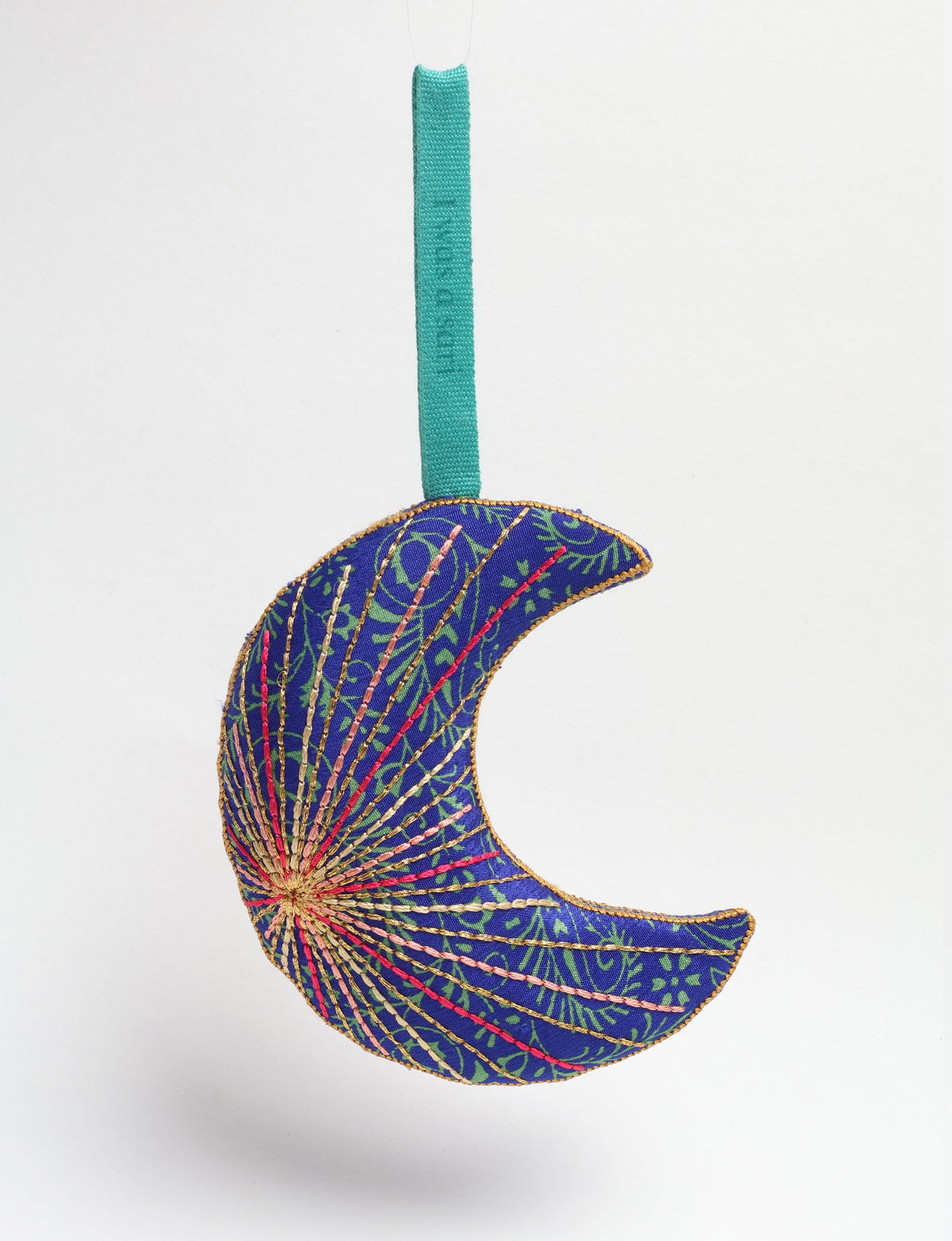 Blue fabric crescent moon ornament with green tropical pattern and multicolored stitched details, hanging by teal loop