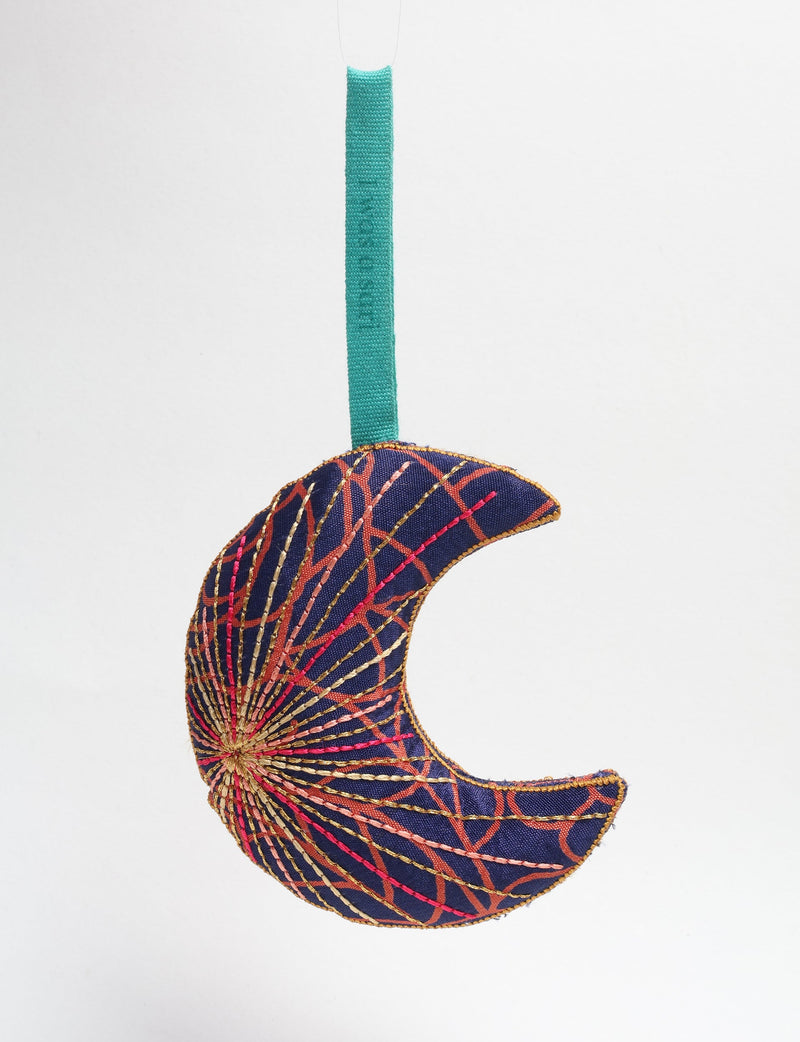 Blue fabric crescent moon ornament with abstract red and gold stitched lines, hanging by a teal loop