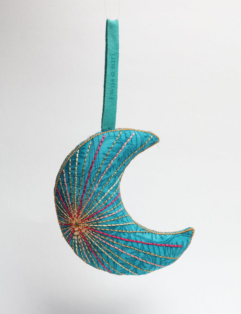 Blue fabric crescent moon ornament with multicolored stitched lines and a matching blue hanging loop against white background