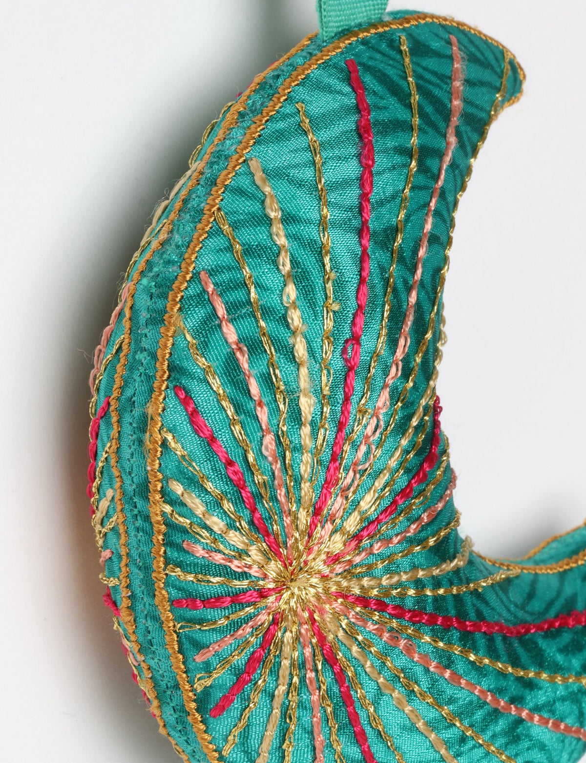 Blue fabric crescent moon ornament with multicolored stitched lines and a matching blue hanging loop against white background