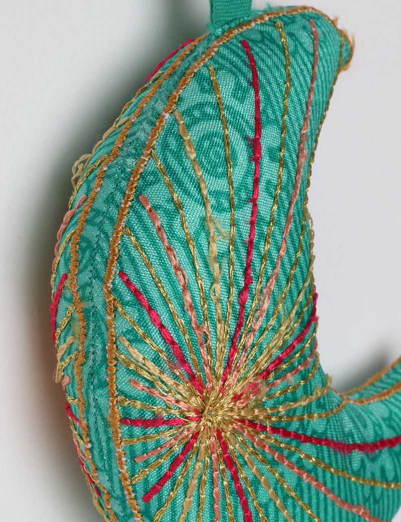 Blue fabric crescent moon ornament with multicolored stitched lines and a matching blue hanging loop against white background