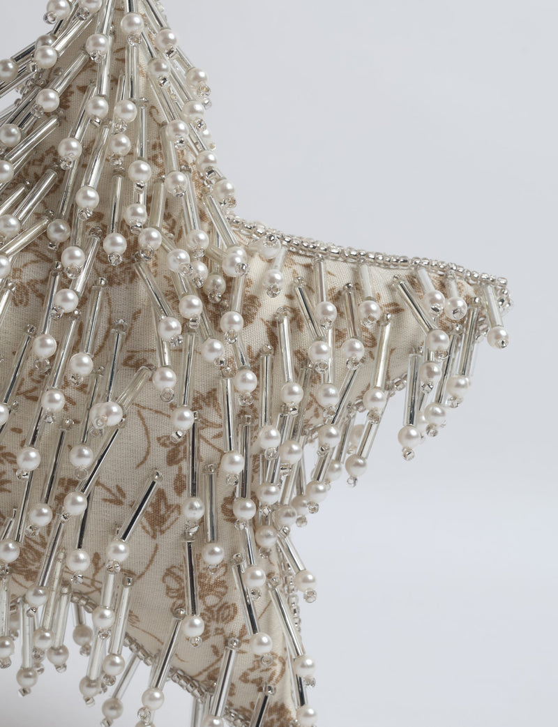 Beige fabric star ornament with brown tropical print, decorated with silver tubes and pearl beads, close-up view
