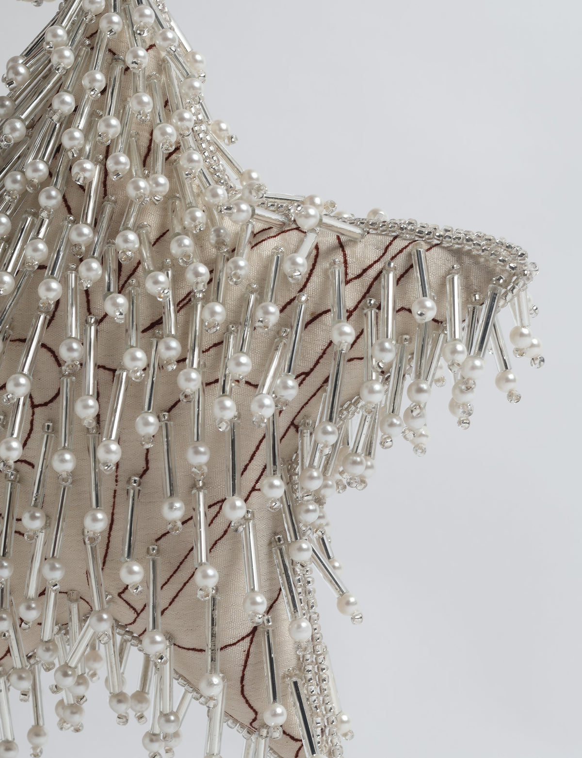 Beige fabric star ornament with silver beads, pearl-like round beads, and brown floral embroidery, close-up view