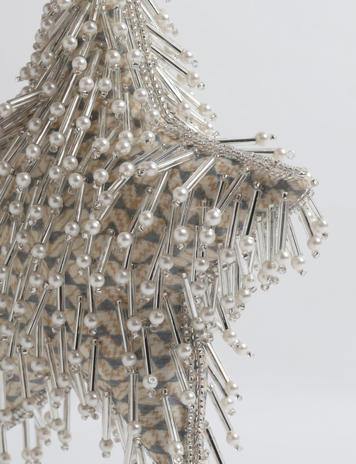 Silver star ornament with beige patterned fabric base, decorated with clear tubes and pearl-like beads, close-up view