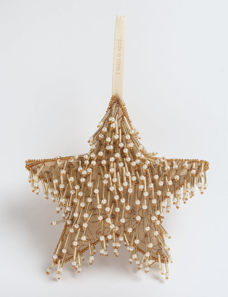 Beige fabric star ornament decorated with gold beads and white pearl-like beads, hanging by a beige ribbon with text