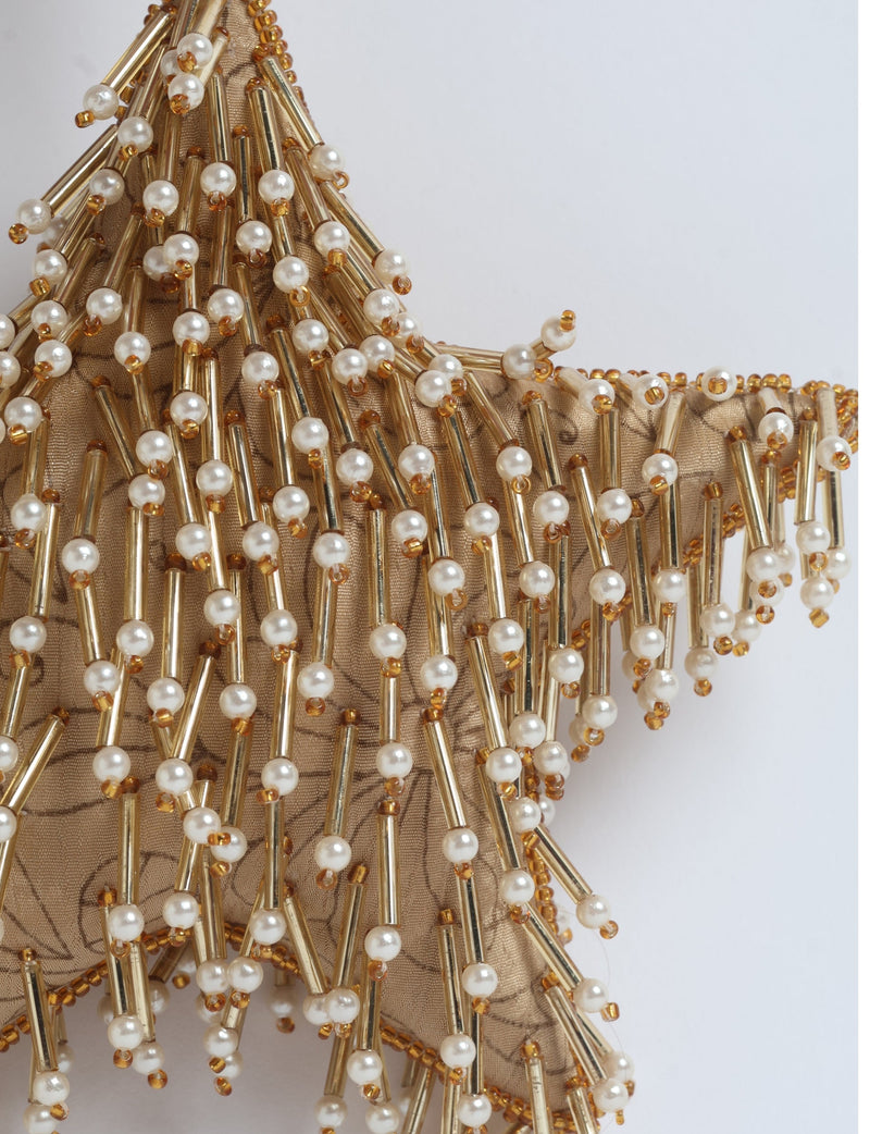Gold star ornament with beige floral fabric base decorated with gold tubes and white pearl beads, close-up view